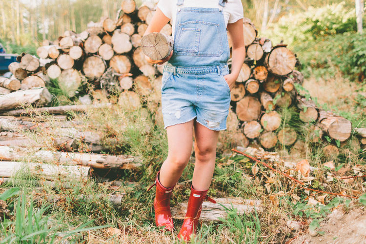 Low section of girl carrying log while standing on field