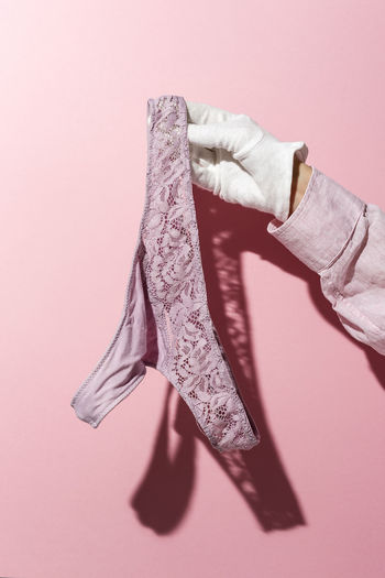 Close-up of hand holding purple panty against pink background