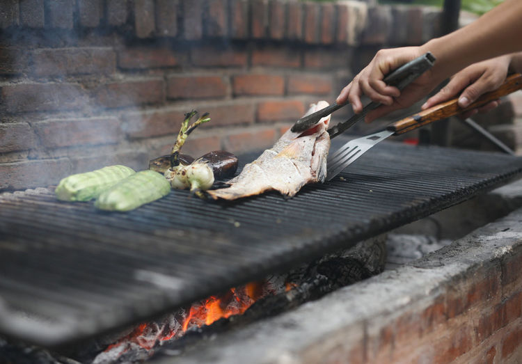 Close-up of man preparing fish on barbecue grill