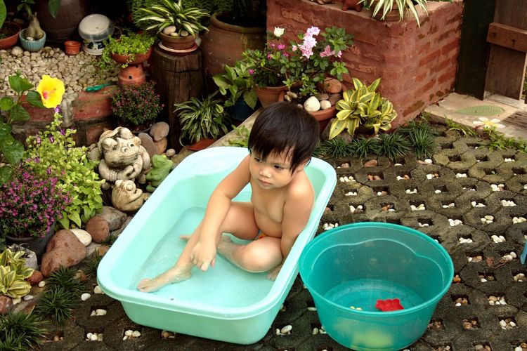 High angle view of shirtless boy sitting in bucket at yard