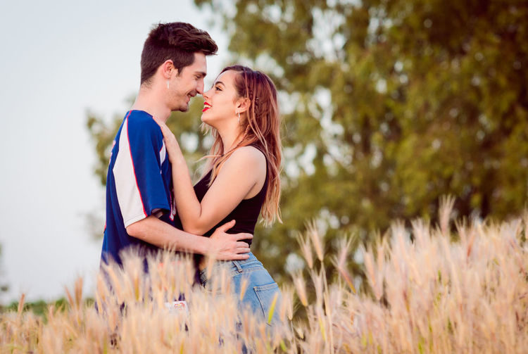Loving young couple standing against sky on field