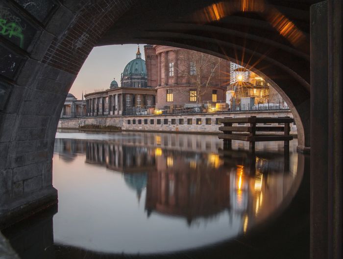 Reflection of arch bridge over river in city