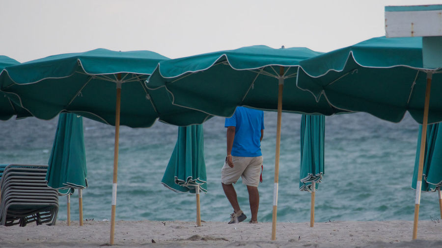 Rear view of man walking by parasols at beach