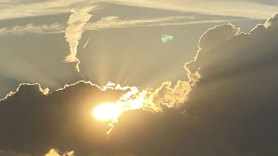 Low angle view of sunlight streaming through clouds during sunset