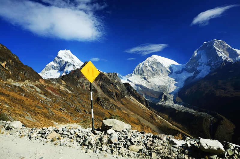 Yellow sign post by stones with mountain peak in background