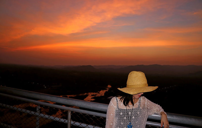 Woman standing in hat against orange sky during sunset