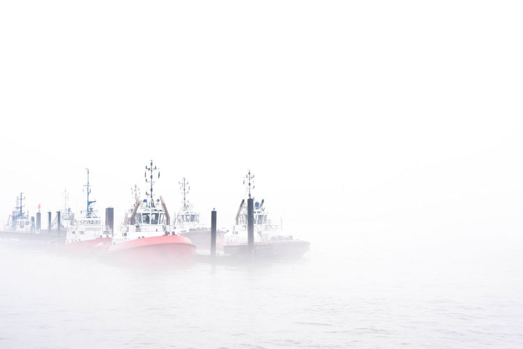 Boats moored at harbor against clear sky