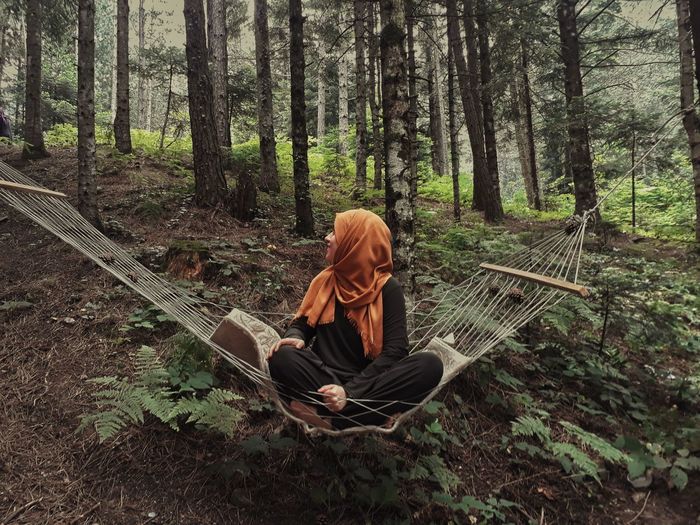 Full length of woman sitting on hammock in forest