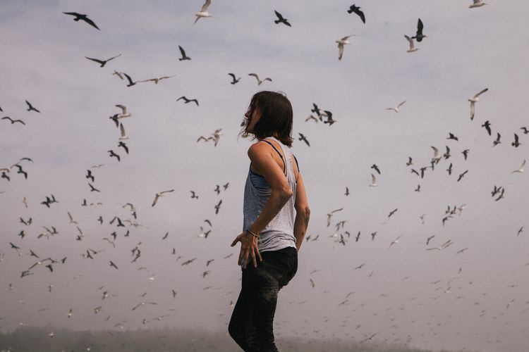 Side view of woman standing against birds