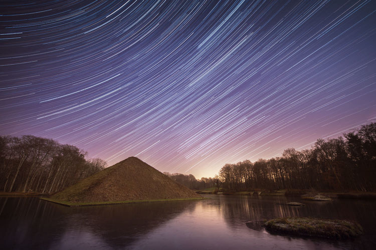 Scenic view of lake against star trails in sky at night