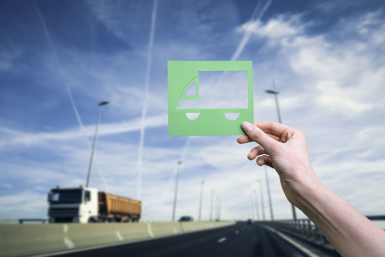 Hand holds green logistics truck symbol against highway
