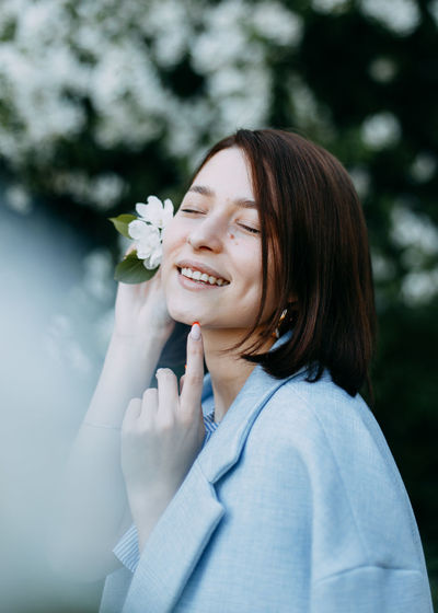 Portrait of happy smiling young woman with flower near her head in blooming park