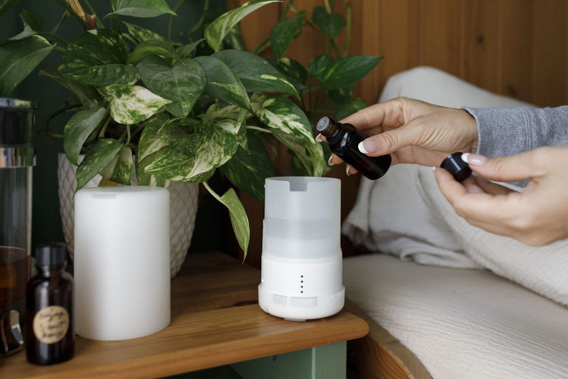 Hand of woman pouring essential oil in air diffuser at home