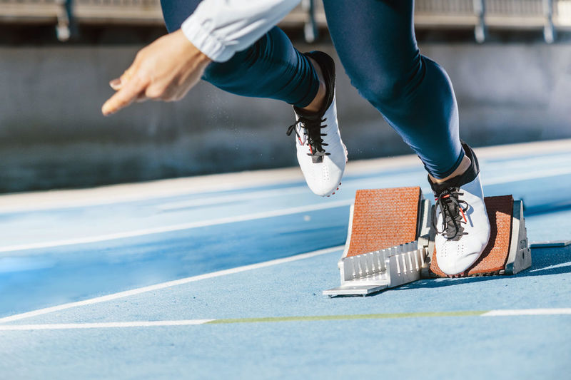 Cropped unrecognizable sportswoman beginning to run fast from starting blocks during track and field workout on stadium