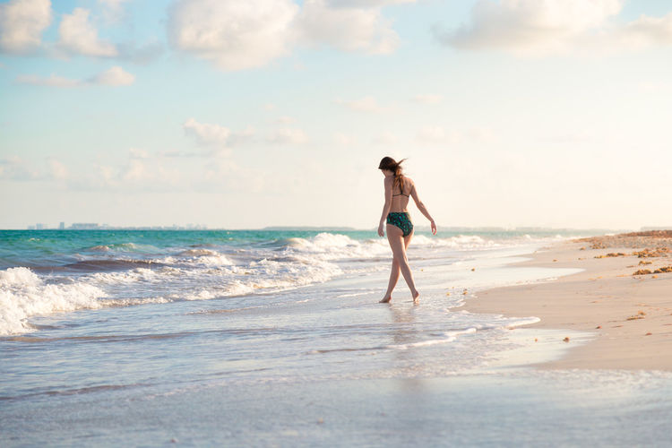 Rear view of woman wearing bikini while walking at beach against sky