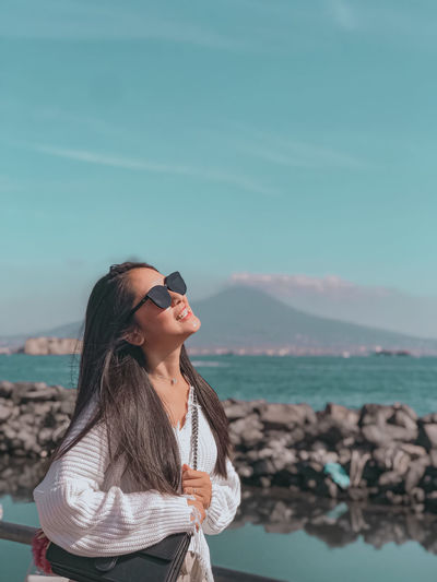 Young woman wearing sunglasses standing against sea