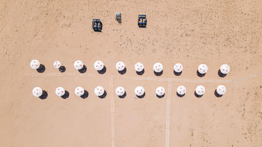 An empty clean sandy beach with two rows of parasols and cabanas, aerial view. 
