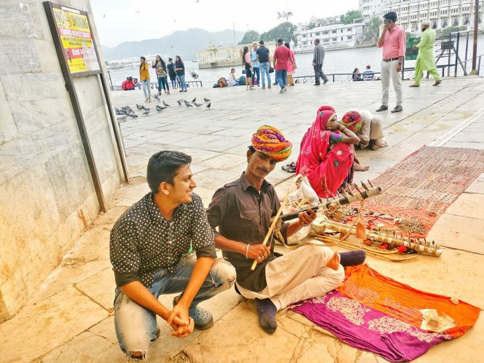 Man sitting by street performer in city