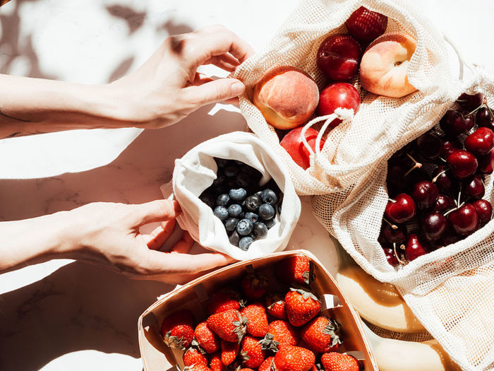 Women's hands are holding textile bags with fruit on the table in sunlight. top view