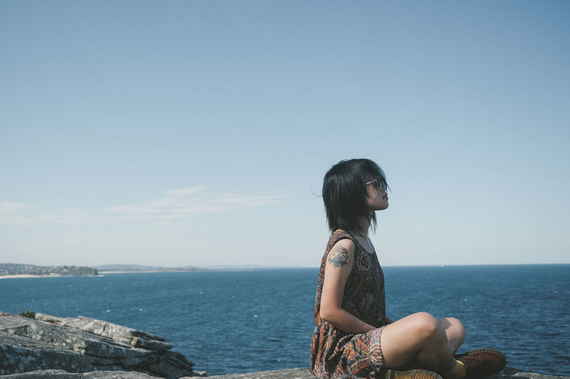 Side view of young woman looking at sea against clear sky