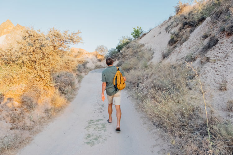 Handsome man in green shirt with a backpack hiking in a mountains. back view.