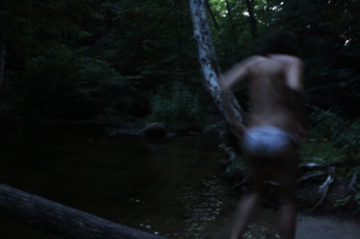 Blur image of shirtless man walking by stream in forest