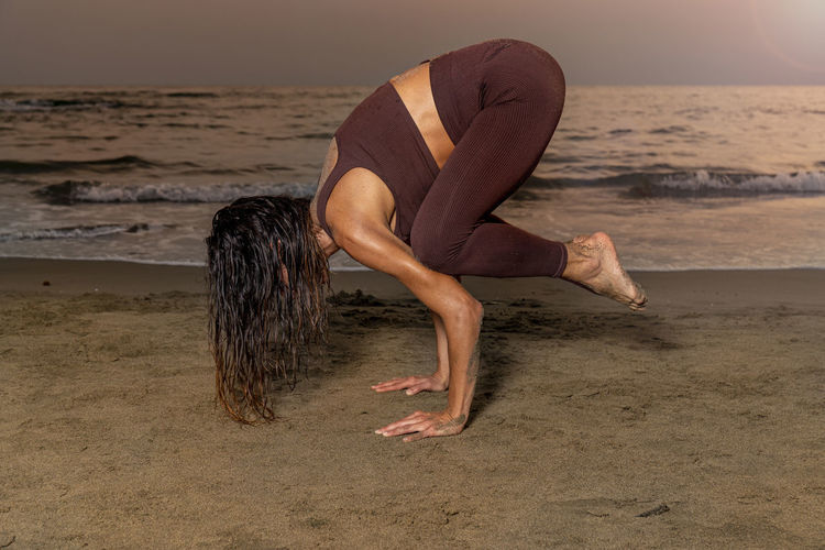 Woman practicing yoga on the beach at sunset. kakasana position for concentration in the present.