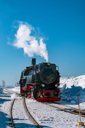 Train on railroad tracks by snowcapped mountain against sky