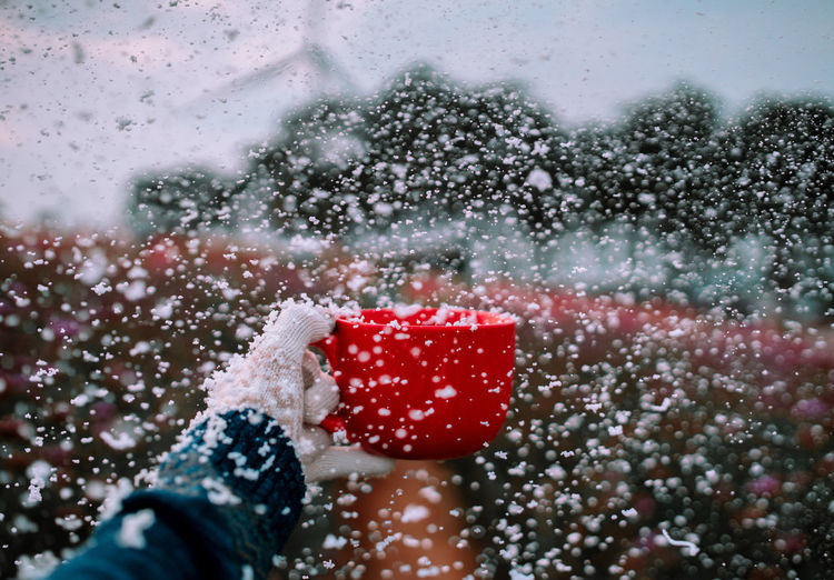 Cropped hand holding red cup while catching snow during snowfall