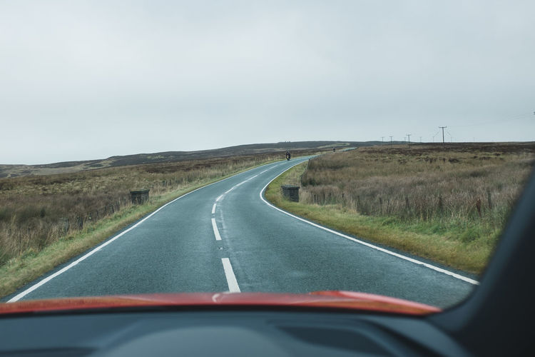 Road by landscape against sky seen through car windshield