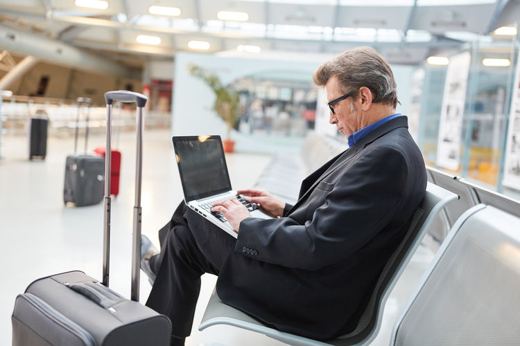 Side view of businessman using laptop while sitting at airport
