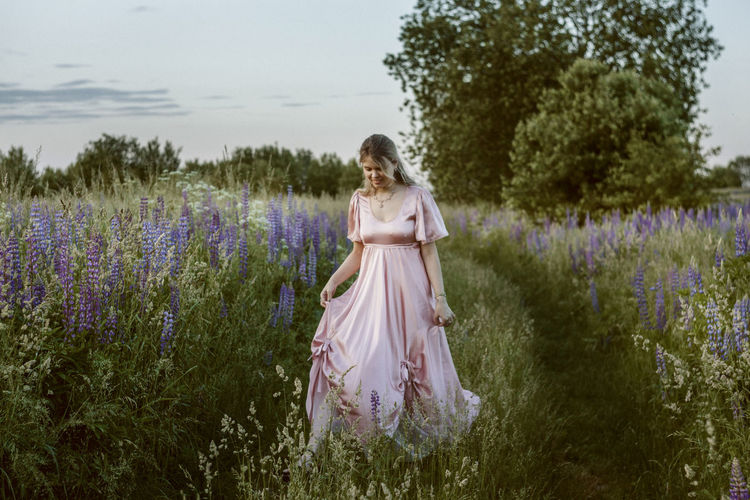 WOMAN STANDING ON FIELD WITH PURPLE FLOWERS IN BACKGROUND