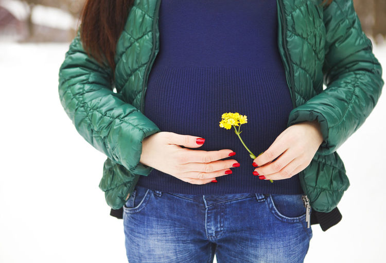 Midsection of pregnant woman holding flowering plant outdoors