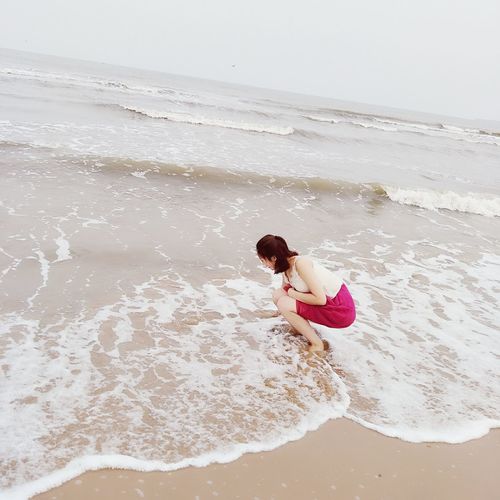 Rear view of young woman on beach against sky