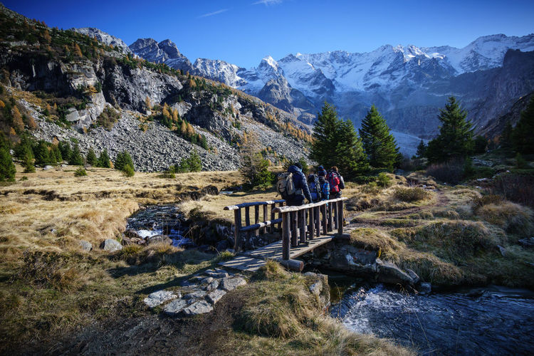 Hikers walking on footbridge over river against mountains