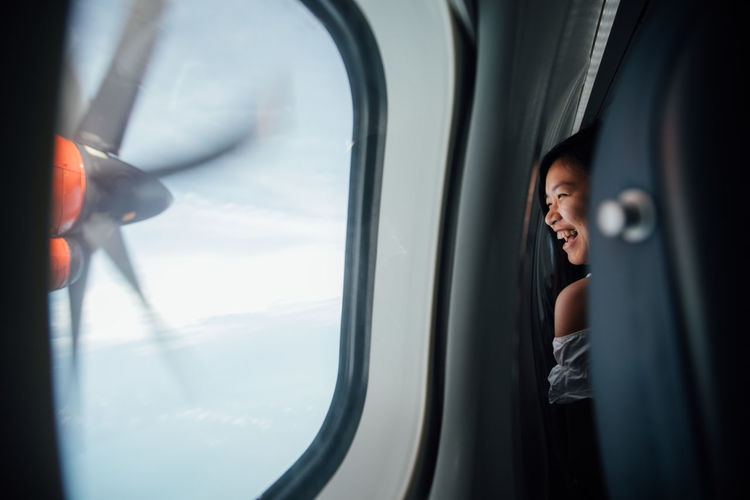 Happy young woman looking through window in airplane
