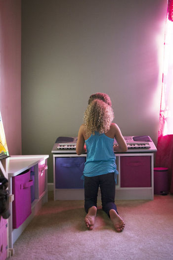 Rear view of girl playing piano at home