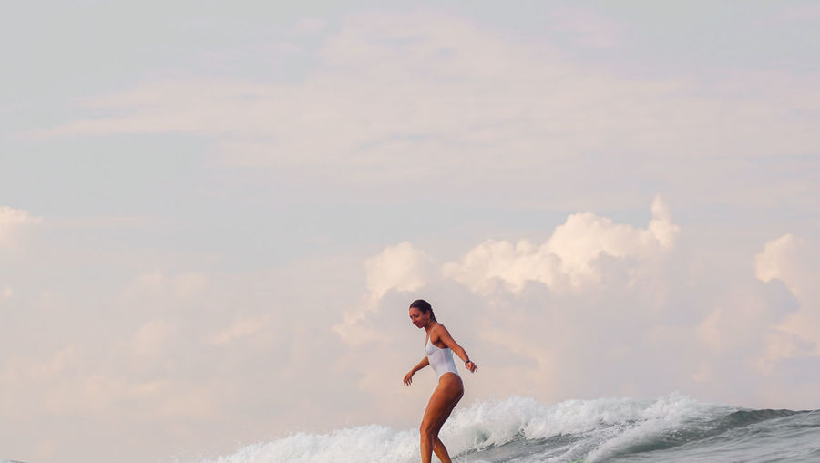 Side view of young woman surfing on sea against sky