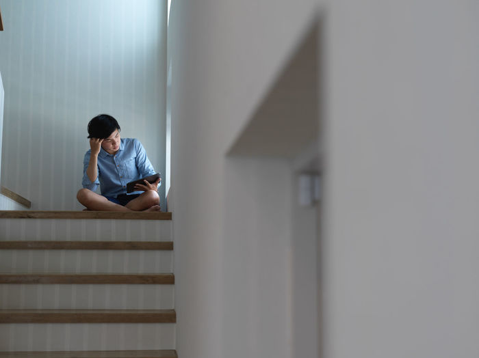 Low angel view of young man holding digital tablet sitting on staircase