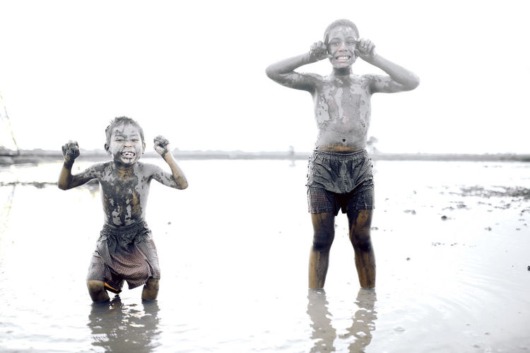 Full length of boy playing in muddy water against clear sky