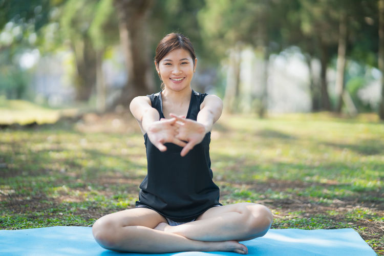 Full length of young woman stretching while sitting at park