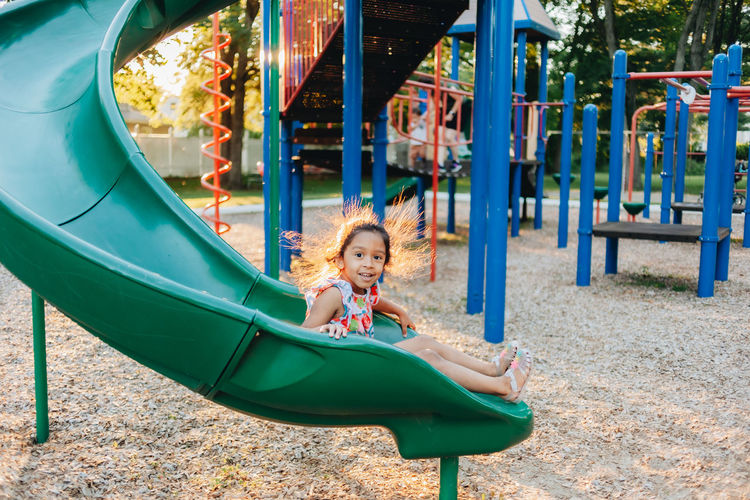 Diverse mixed race pre school girl outdoors during summer having fun at playground park 