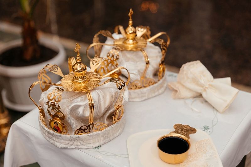 Golden crown of white fabric with a pattern lie on a table next to a golden cup