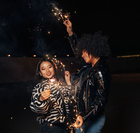 Smiling women holding sparkler standing outdoors