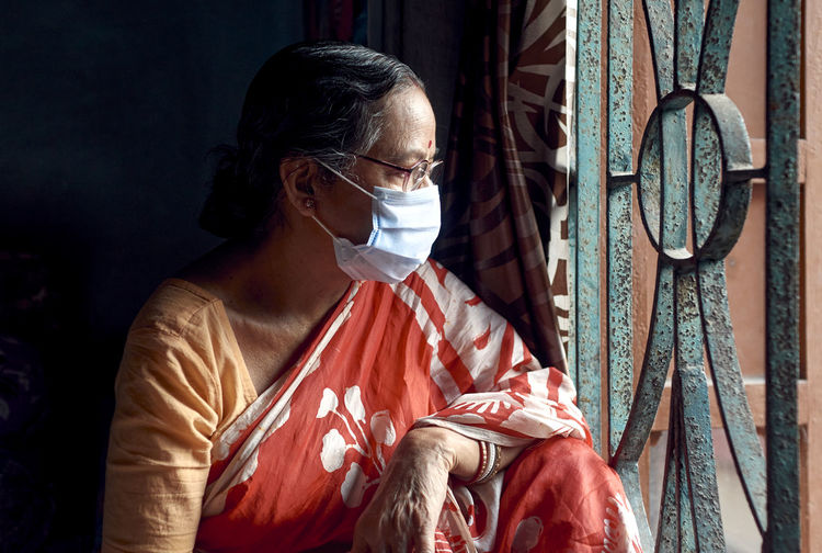 Portrait of an aged indian woman looking outside from her room window during covid-19 pandemic
