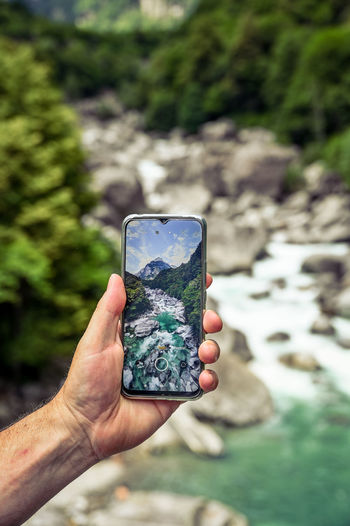 Man holding a mobile phone over turquoise mountain river scenery 