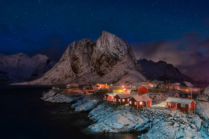 Illuminated stilt houses by lake and mountains during winter at night