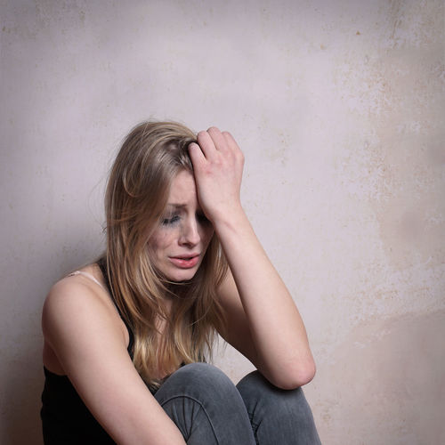 Sad young woman sitting by wall at home