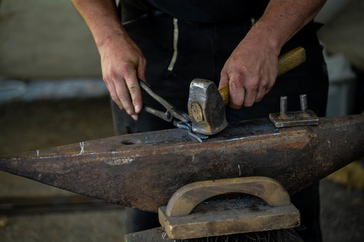 Midsection of man hammering horseshoe on anvil in workshop