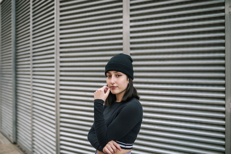 Confident young woman in knit hat against metallic shutter